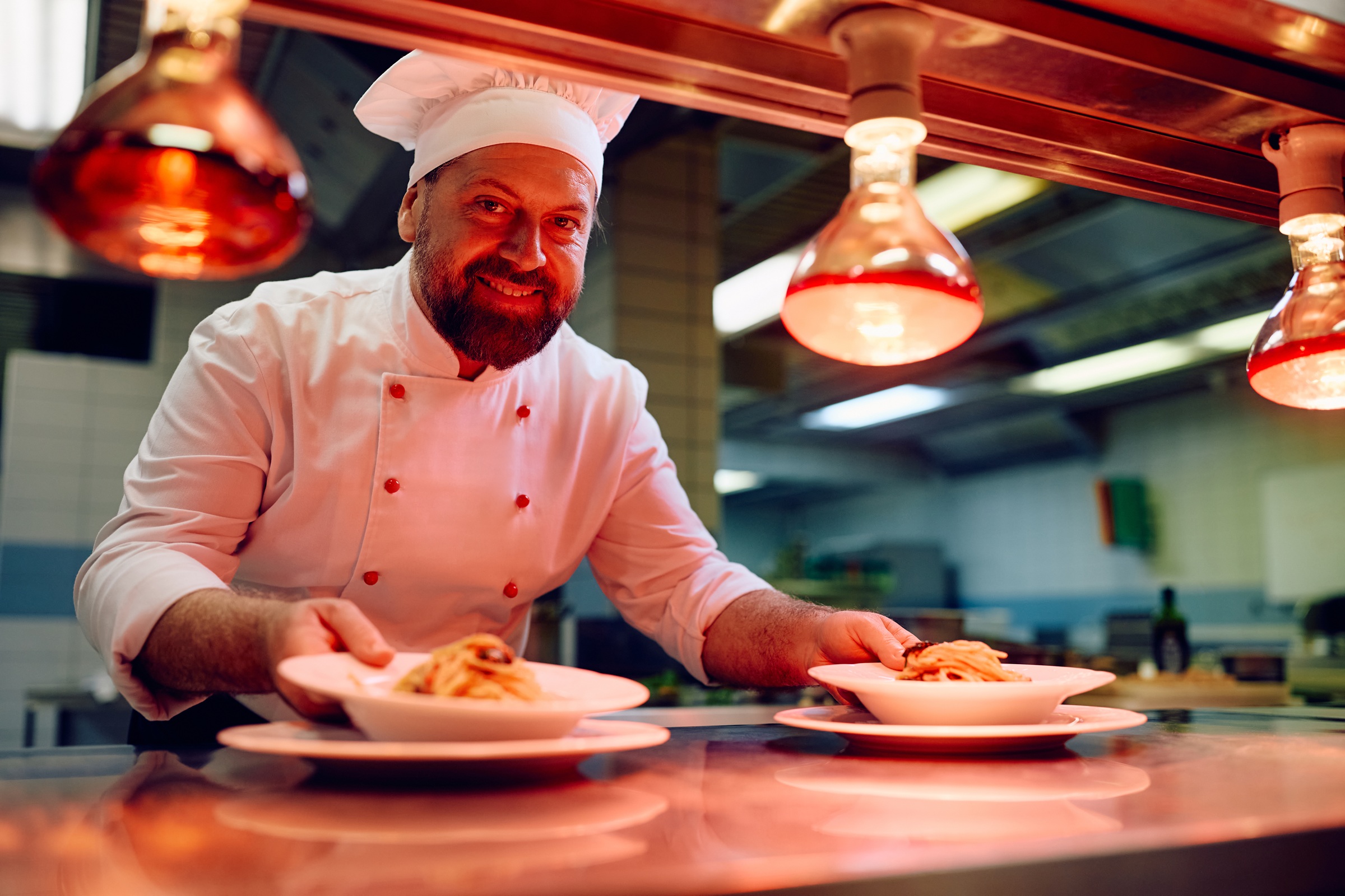 Happy chef serving ordered dish on kitchen counter in a restaurant and looking at camera.